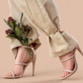 Legs of young woman in stylish high heels with beautiful flowers on brown background