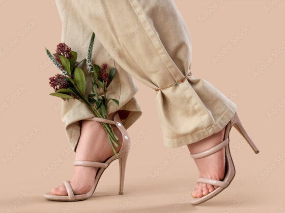Legs of young woman in stylish high heels with beautiful flowers on brown background