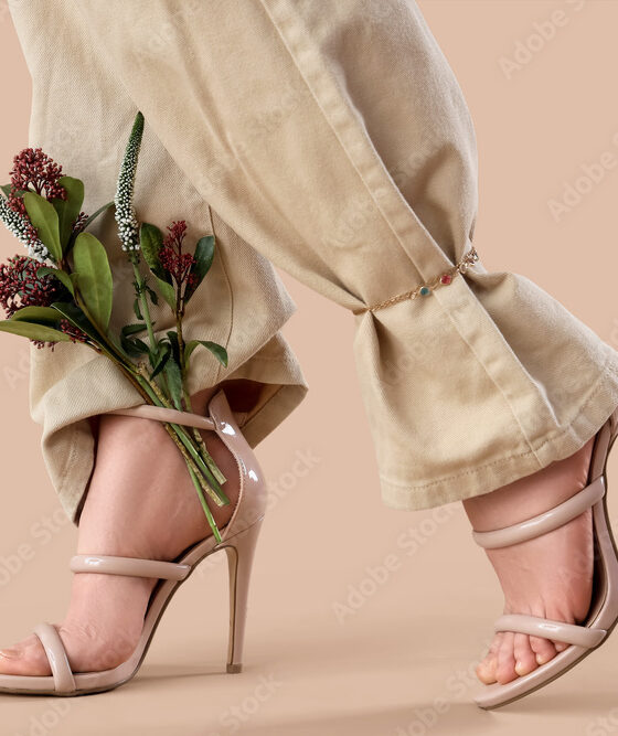 Legs of young woman in stylish high heels with beautiful flowers on brown background