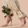 Legs of young woman in stylish high heels with beautiful flowers on brown background