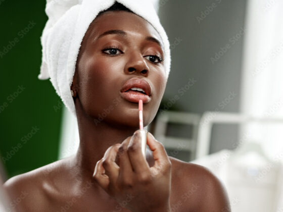 Woman applying lip gloss in a beauty routine at home during the daytime with natural light illuminating her face