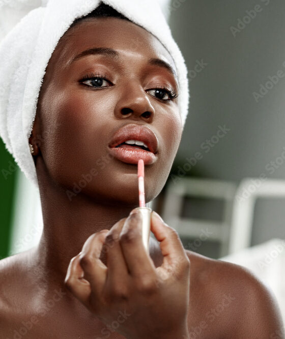 Woman applying lip gloss in a beauty routine at home during the daytime with natural light illuminating her face