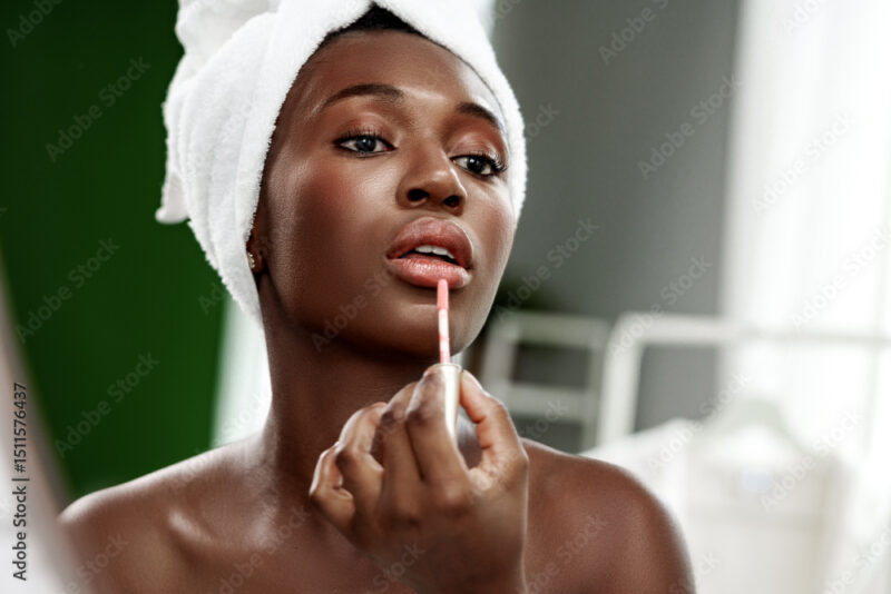 Woman applying lip gloss in a beauty routine at home during the daytime with natural light illuminating her face