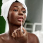 Woman applying lip gloss in a beauty routine at home during the daytime with natural light illuminating her face